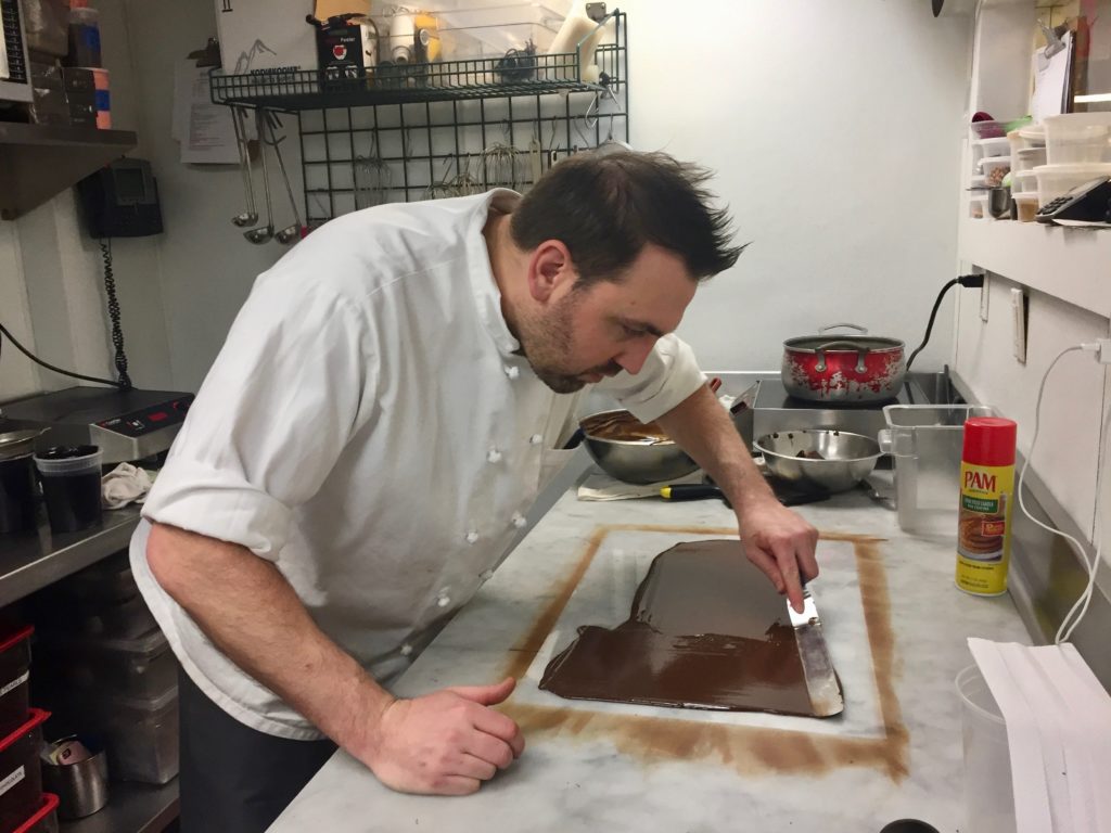 Tyler Atwell smooths out the chocolate he is tempering before cutting it and letting it harden. Credit: Lisa Kocay. 